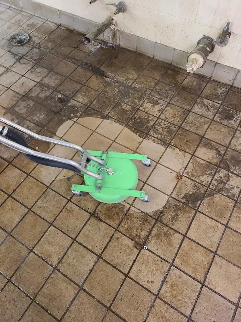 Commercial kitchen tile floor with one cleaned patch in heavy soil under a cleaning tool