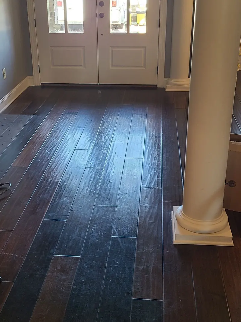 Dark hand-scraped hardwood floor at a front entry with dull traffic wear