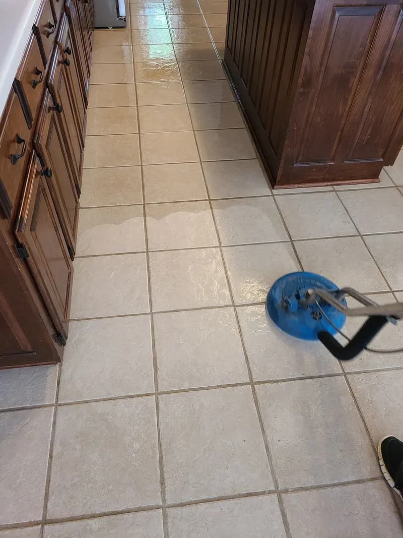 Kitchen tile floor partly cleaned, with the spinner tool working along the cabinets