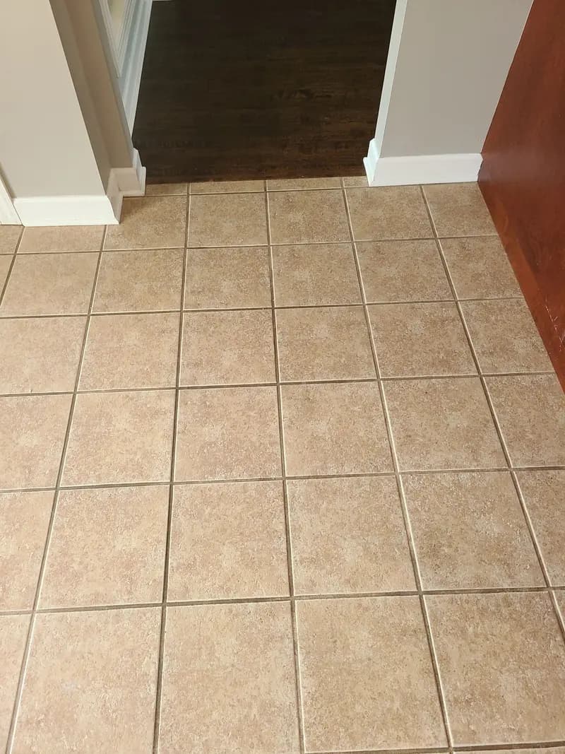 Before: Tan tile floor at a doorway with darkened grout lines before cleaning