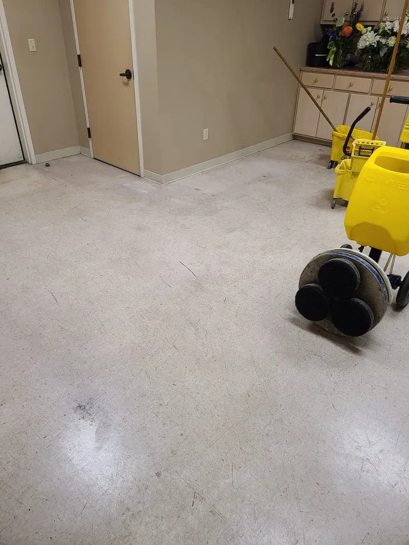 Before: Dull VCT break room floor before stripping, with a floor machine and mop bucket