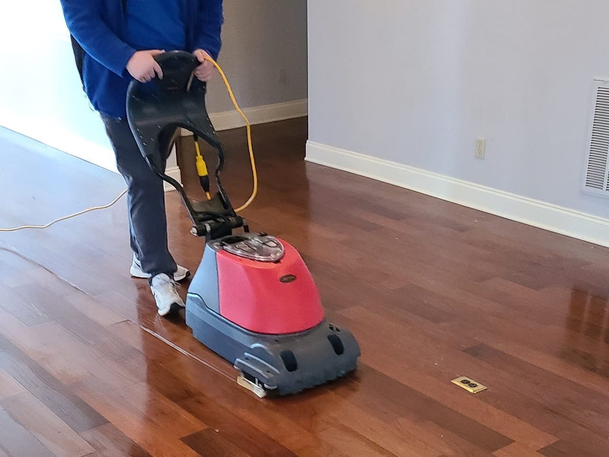 Technician running a floor machine across a cherry hardwood floor
