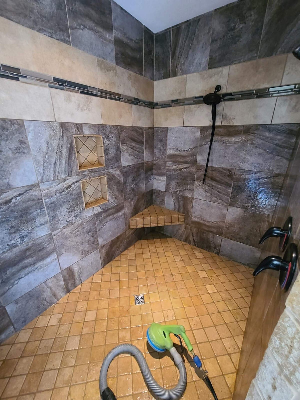 Tiled shower with a spinner cleaning tool and vacuum hose on the small-tile floor