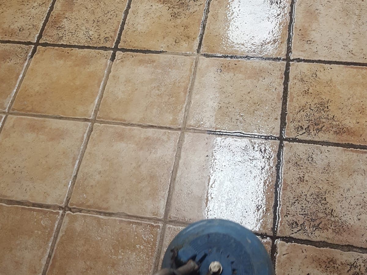 Spinner tool cleaning tan floor tile, with dark grout ahead of it and clean grout behind