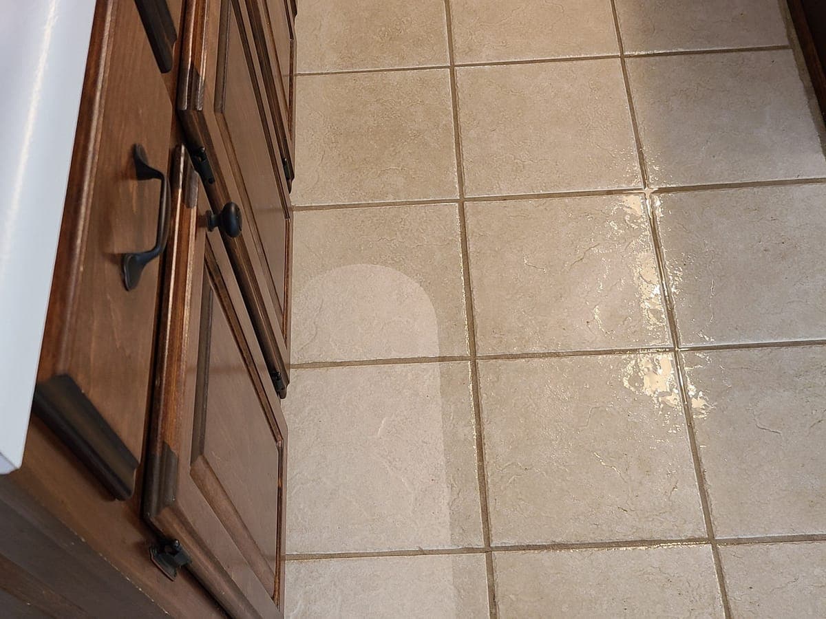 Kitchen tile floor beside wood cabinets, wet, with a lighter cleaned path across it