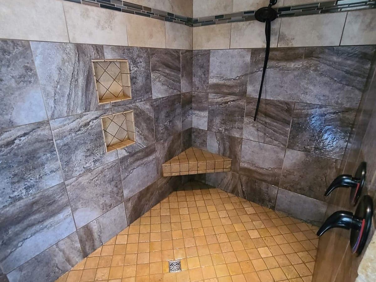 Tiled shower with stone-look wall tile, a bench and a small-tile floor