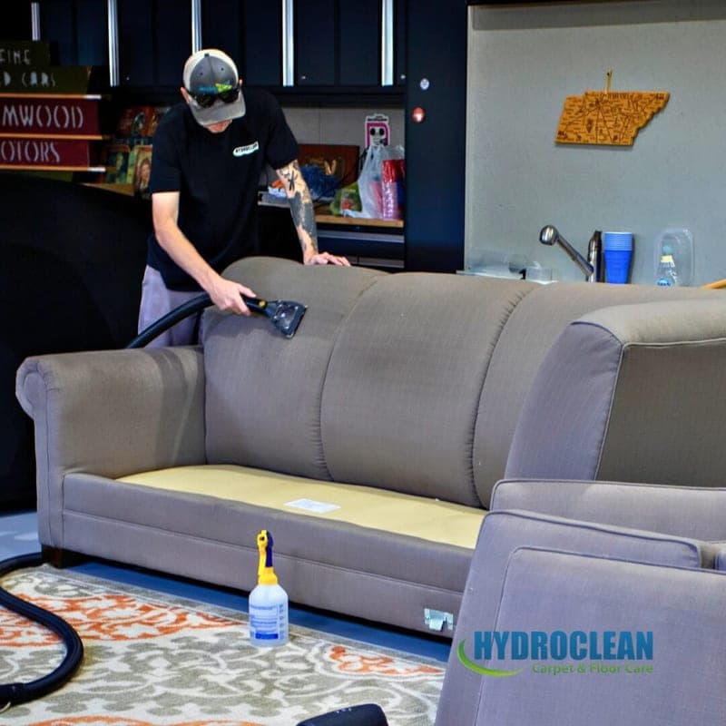 HydroClean technician cleaning a gray sofa with an upholstery hand tool