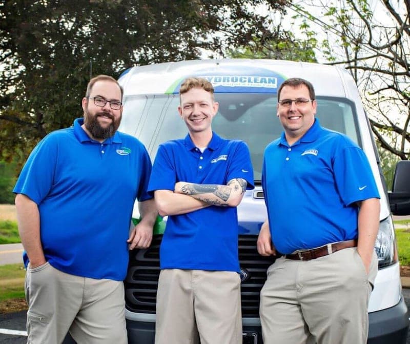 Three HydroClean team members in blue shirts standing in front of the company van
