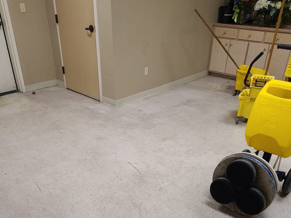 Dull VCT break room floor before stripping, with a floor machine and mop bucket